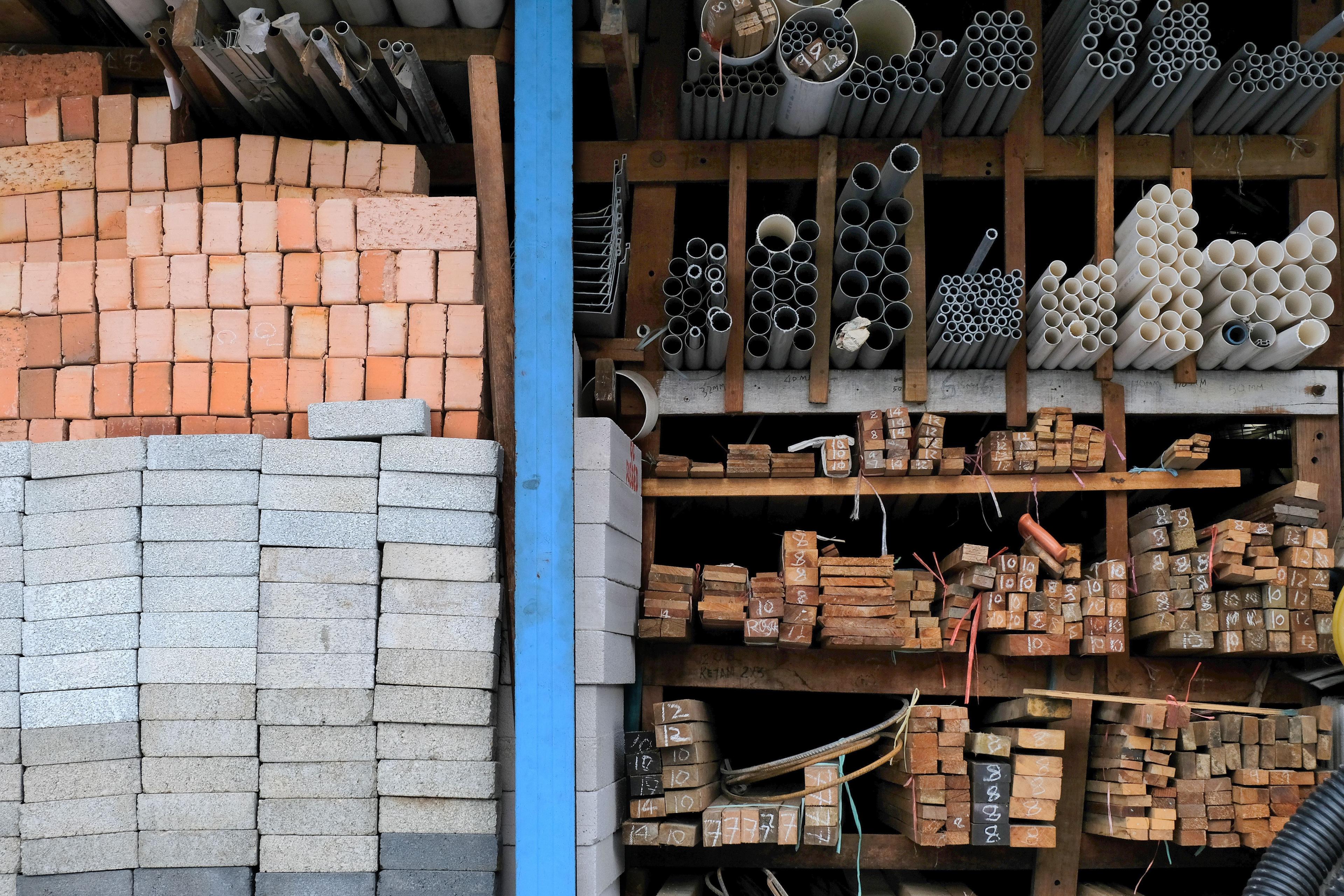 Construction building materials and industrial supplies such as bricks, woods and pipes stacked and arranged for sale at a hardware store front. | Image Credit: © Sweeann - stock.adobe.com