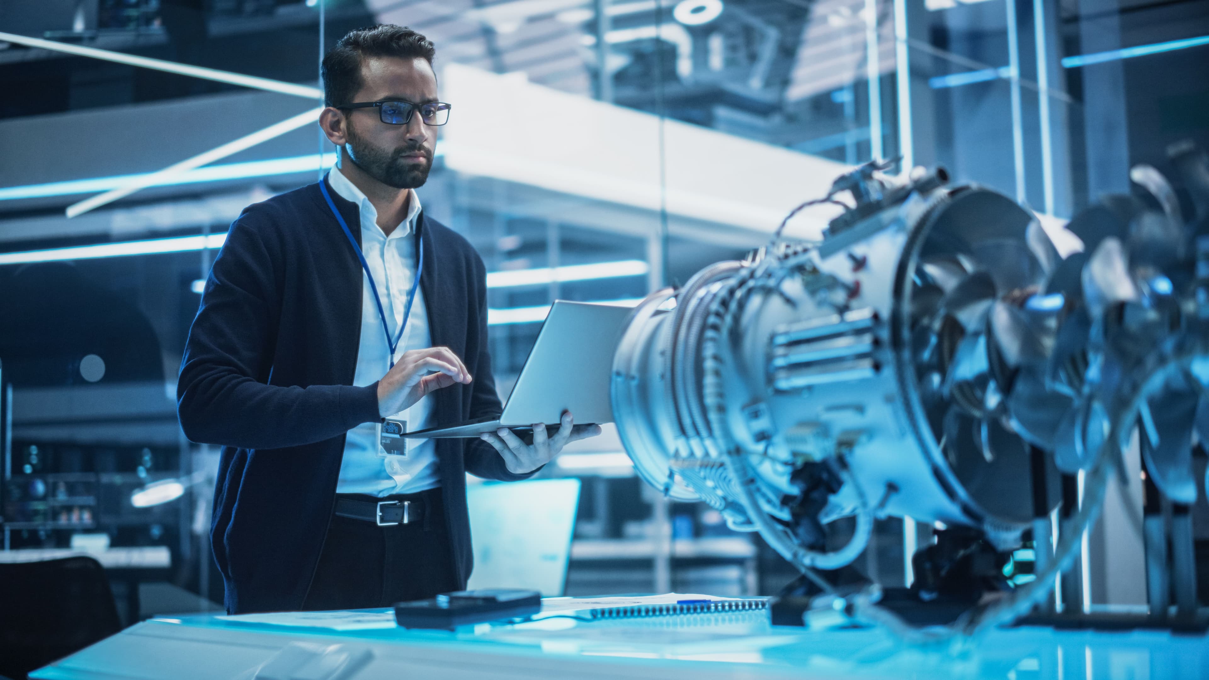 Young Industrial Engineer Working on a Futuristic Jet Engine, Standing with Laptop Computer in Scientific Technology Lab. Scientist Developing a New Electric Motor in a Research Facility. | Image Credit: © Gorodenkoff - stock.adobe.com