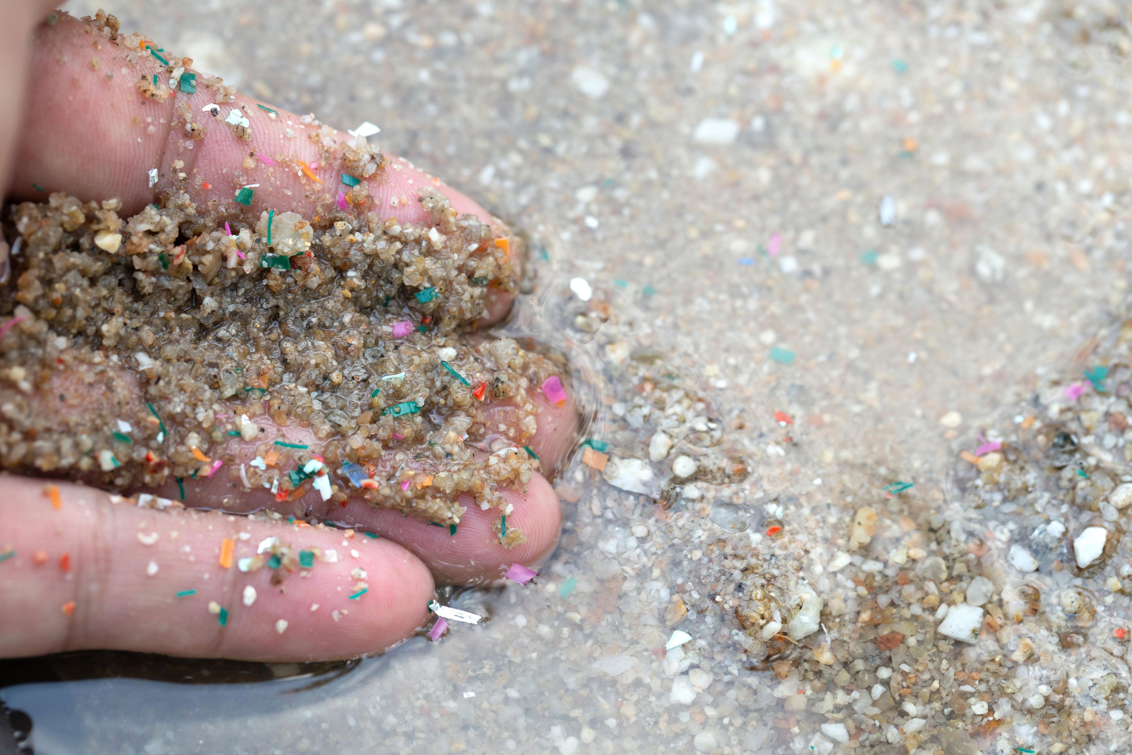 Close-up side shot of hands shows microplastic waste contaminated with the seaside sand. Microplastics are contaminated in the sea. Concept of water pollution and global warming. | Image Credit: © Pcess609 - stock.adobe.com