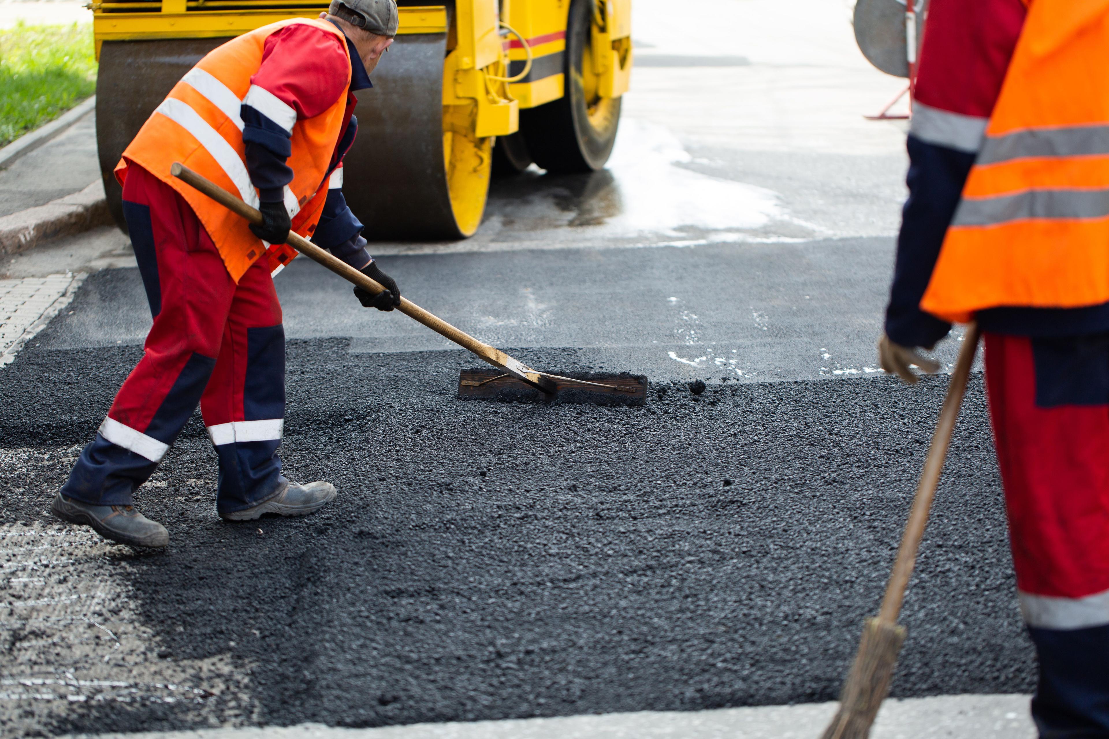 The road workers' working group updates part of the road with fresh hot asphalt and smoothes it for repair. | Image Credit: © Artem Zakharov - stock.adobe.com