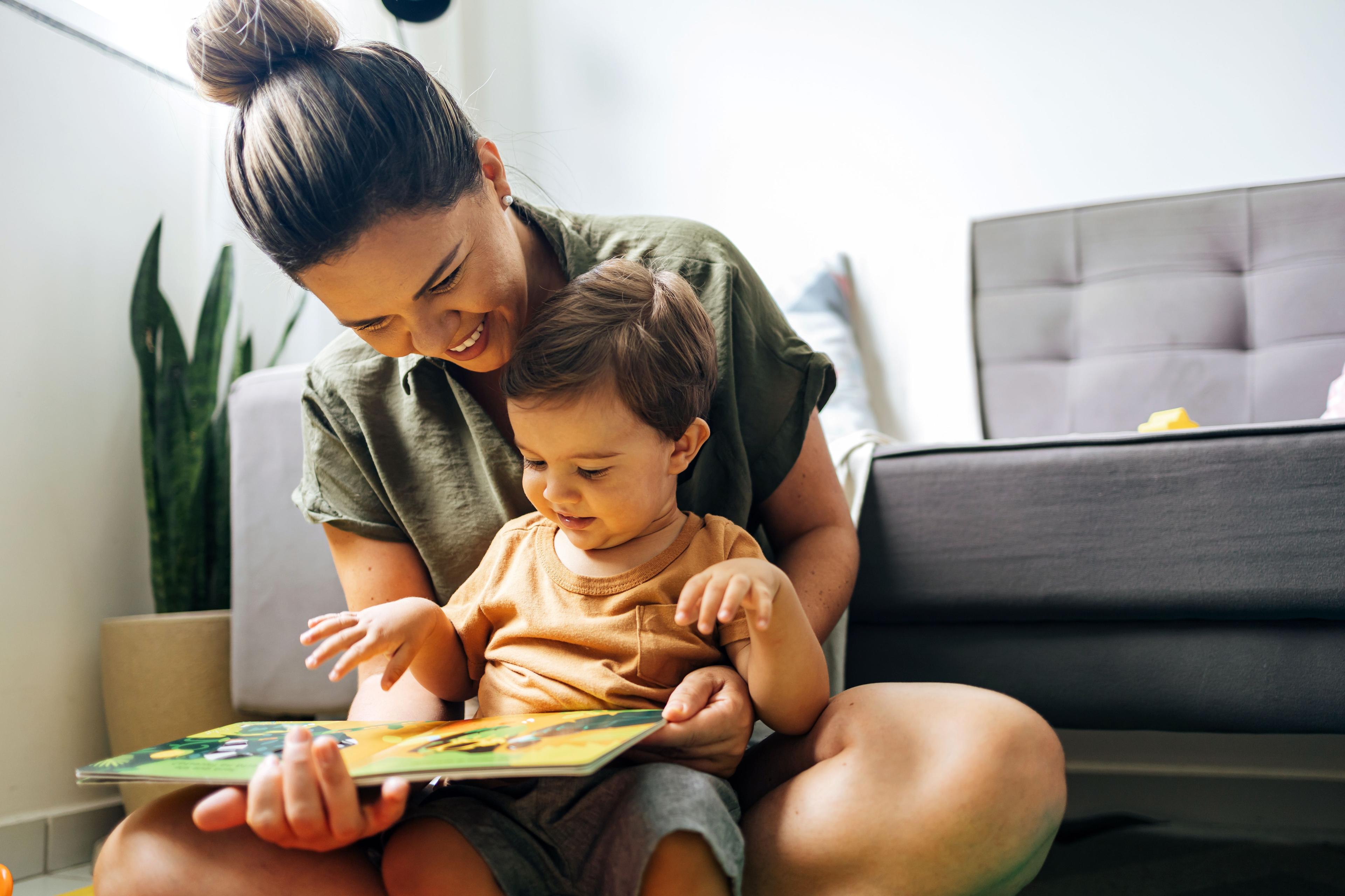 Mom reading a book with baby boy at home. Early age children education, development. Mother and child spending time together. Candid lifestyle. | Image Credit: © kleberpicui - stock.adobe.com